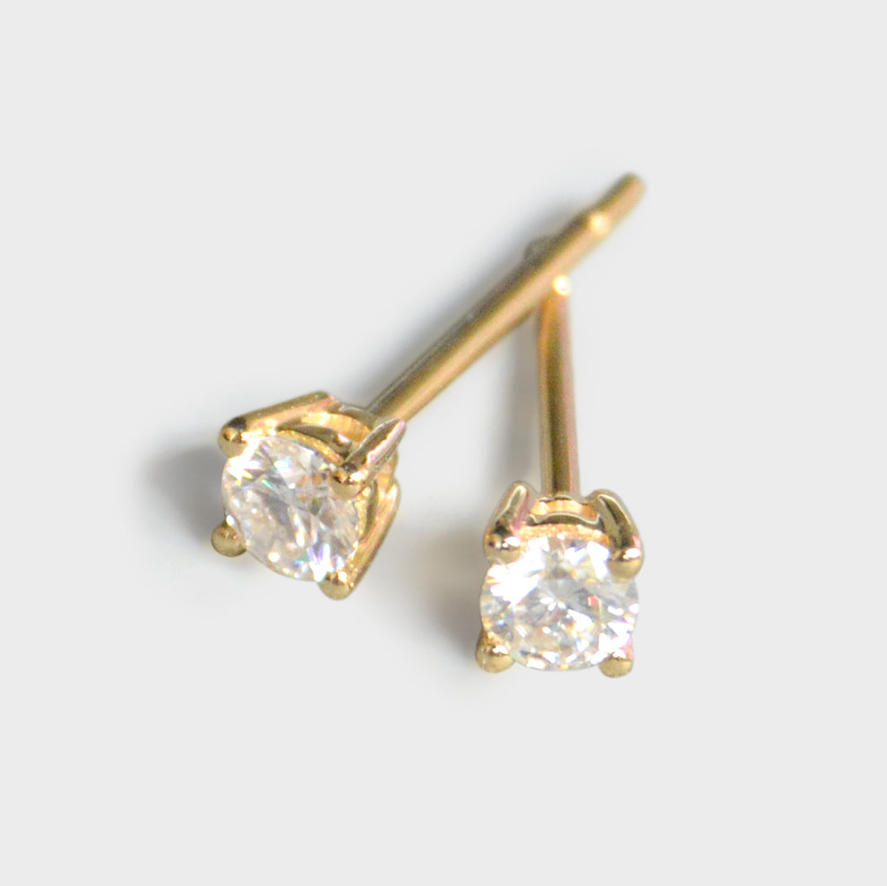 Gold stud earrings with clear gemstones on a light gray background