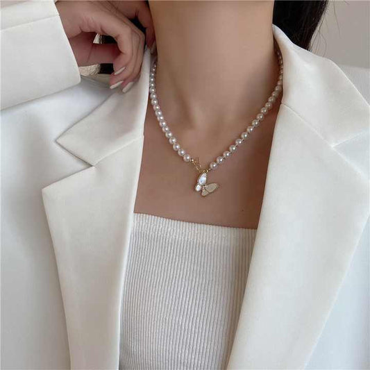 Pearl necklace with a heart pendant worn by a person in a white blazer.