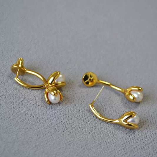 Gold earrings with pearl drops on a gray background