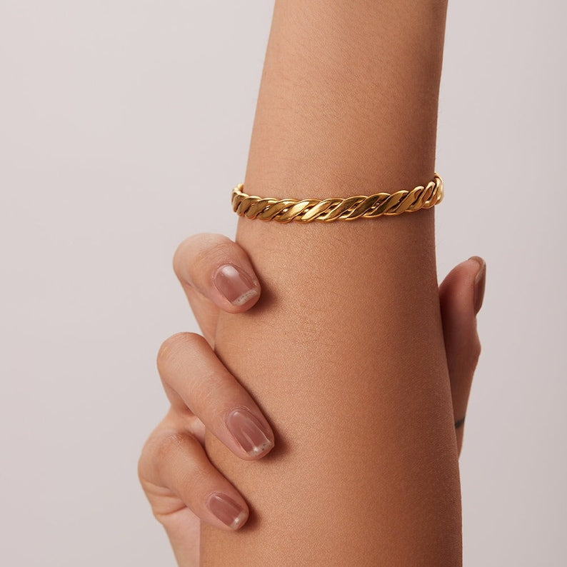 Gold chain bracelet on a wrist against a plain background