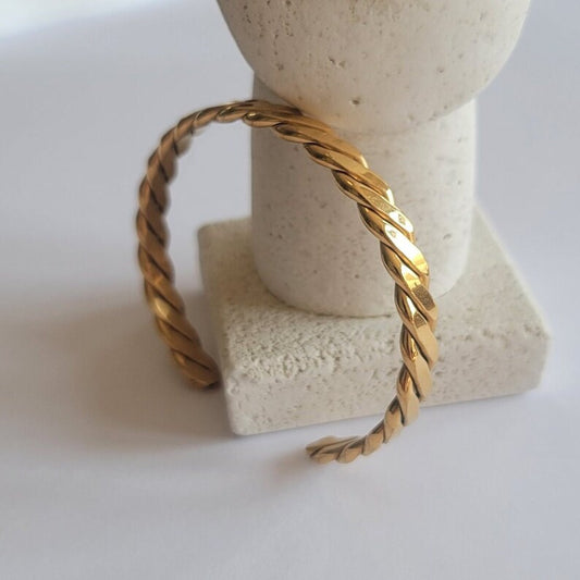 Gold braided bracelet on a stone block with a white background
