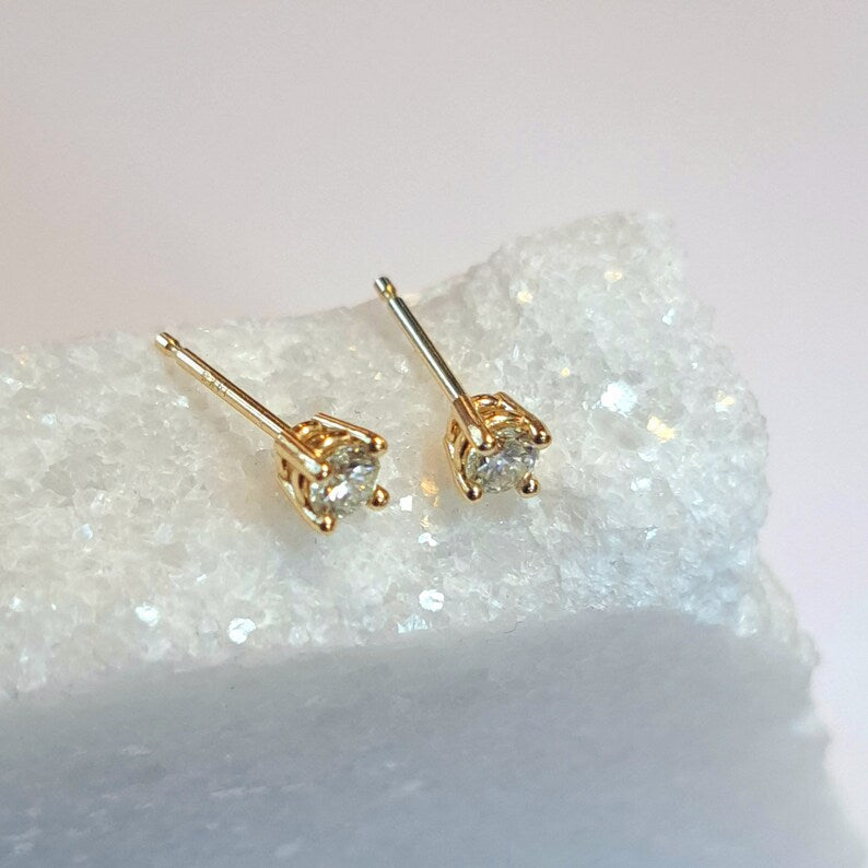 Gold stud earrings with clear gemstones on a textured white surface