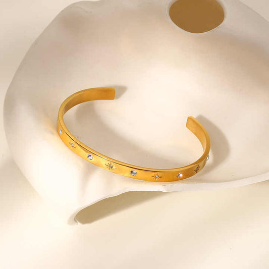 A gold-plated cuff bracelet with cubic zirconia crystals on a white surface.