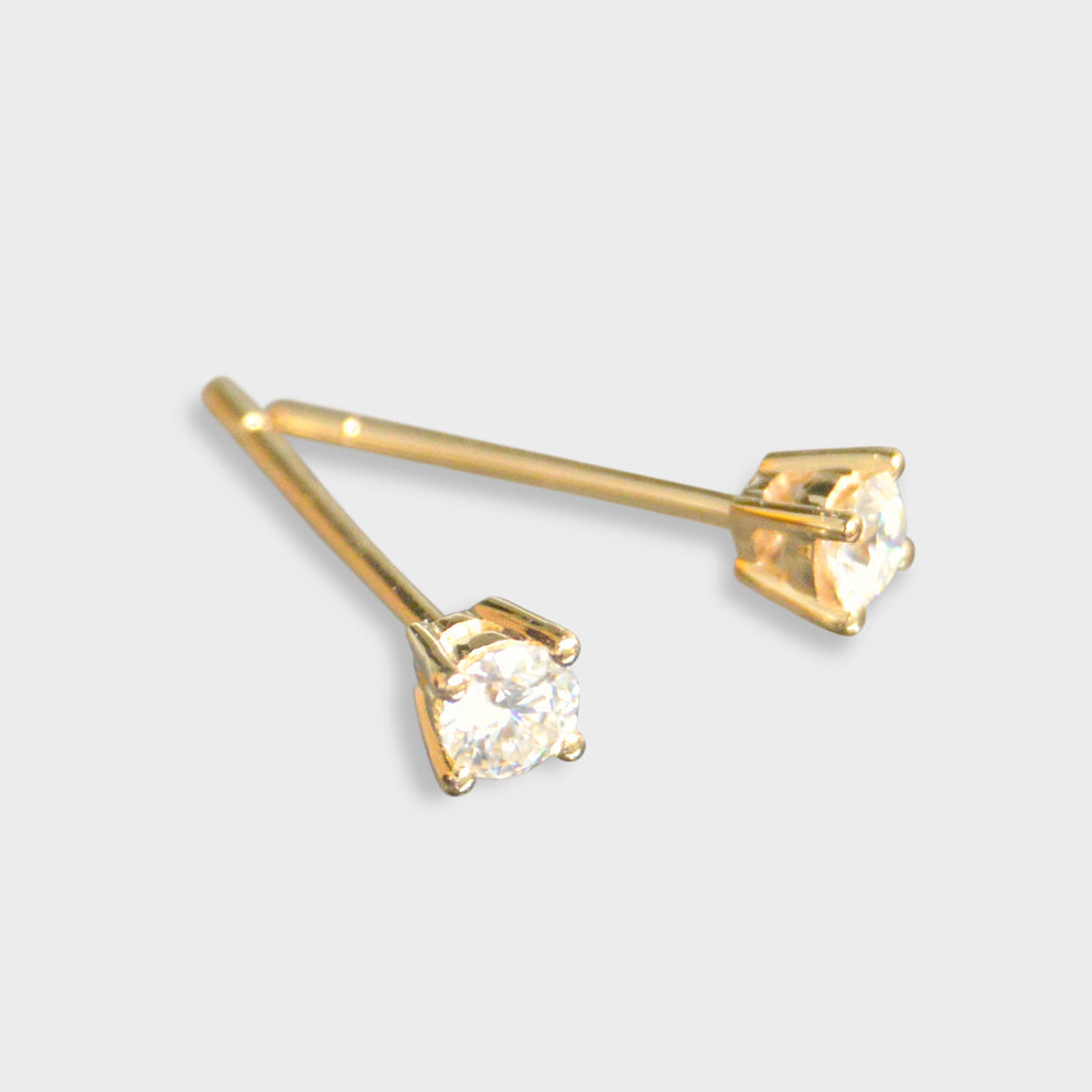 Gold stud earrings with clear gemstones on a light gray background