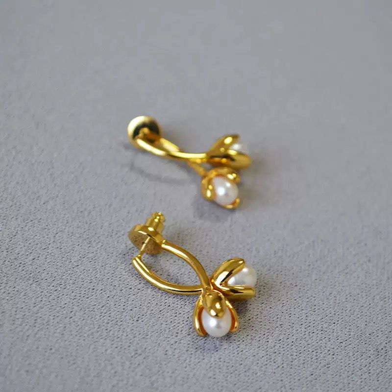 Gold earrings with pearl-like stones on a gray background